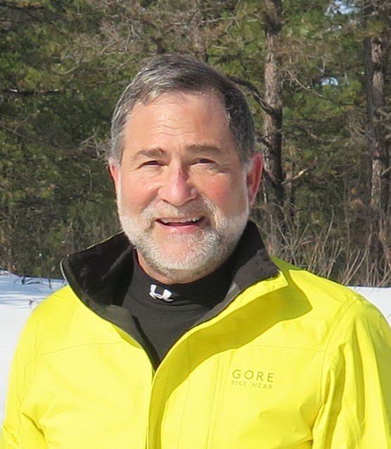 Jim Slavin, grey hair and beard, smiling, wearing yellow coat with black inner lining. Winter scene.
